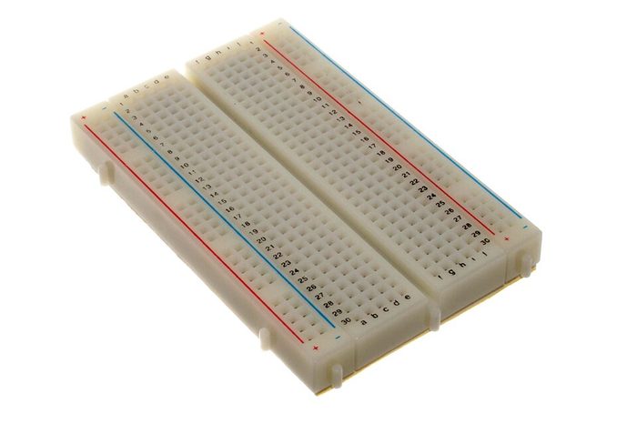 Breadboard putih ukuran sedang dengan garis merah dan biru penanda jalur power di kedua sisi.
