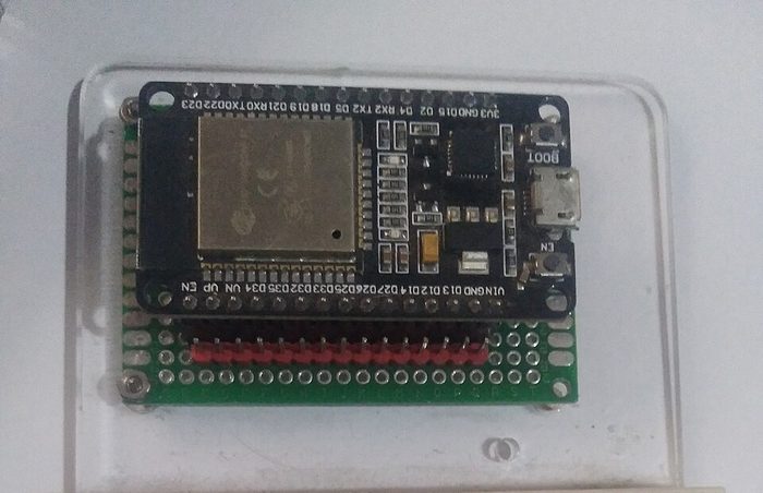 Papan ESP32 DevKit dalam casing akrilik bening, menunjukkan modul ESP32-WROOM, tombol BOOT dan EN, serta port micro USB.