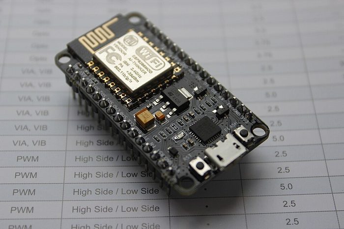 Papan NodeMCU berbasis ESP8266 di atas kertas data sheet, memperlihatkan modul ESP8266MOD, port micro USB, dan dua baris pin header.
