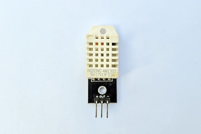 Modul sensor DHT22 (AM2302) berbentuk kotak putih berlubang-lubang dengan tiga pin VCC, OUT, dan GND di bagian bawah.